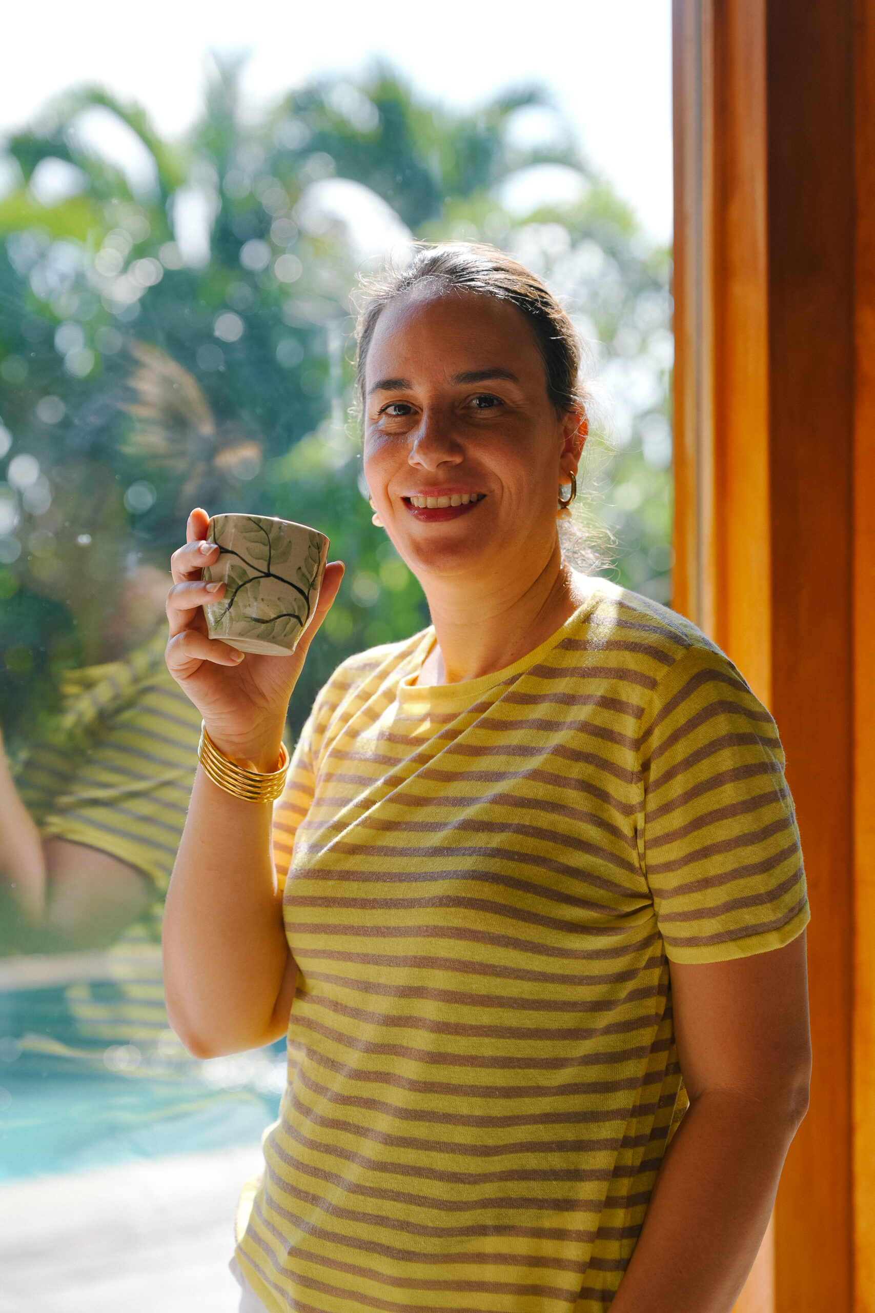 Sophia Benarafa, founder of The Academy by Sophia, smiling with a cup of tea beside a poolside window