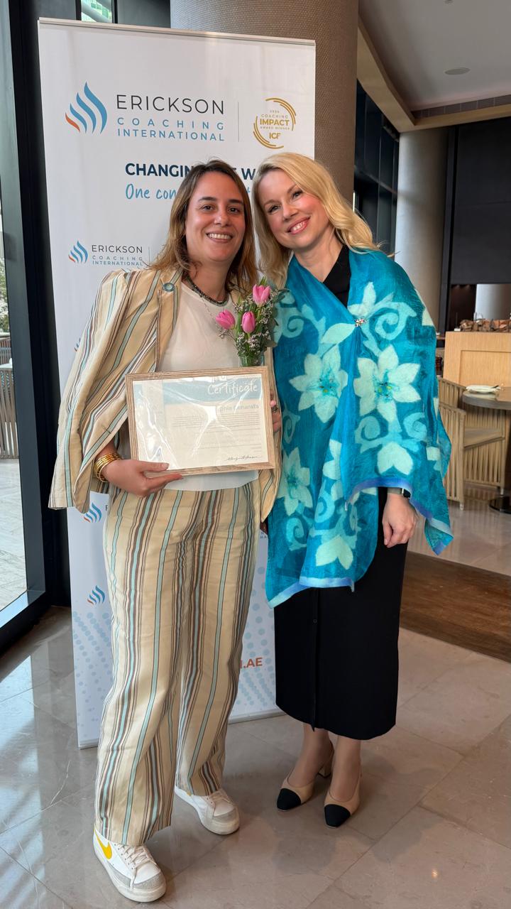 Sophia Benarafa holding her Erickson Coaching International certificate beside a trainer at the certification event in the UAE